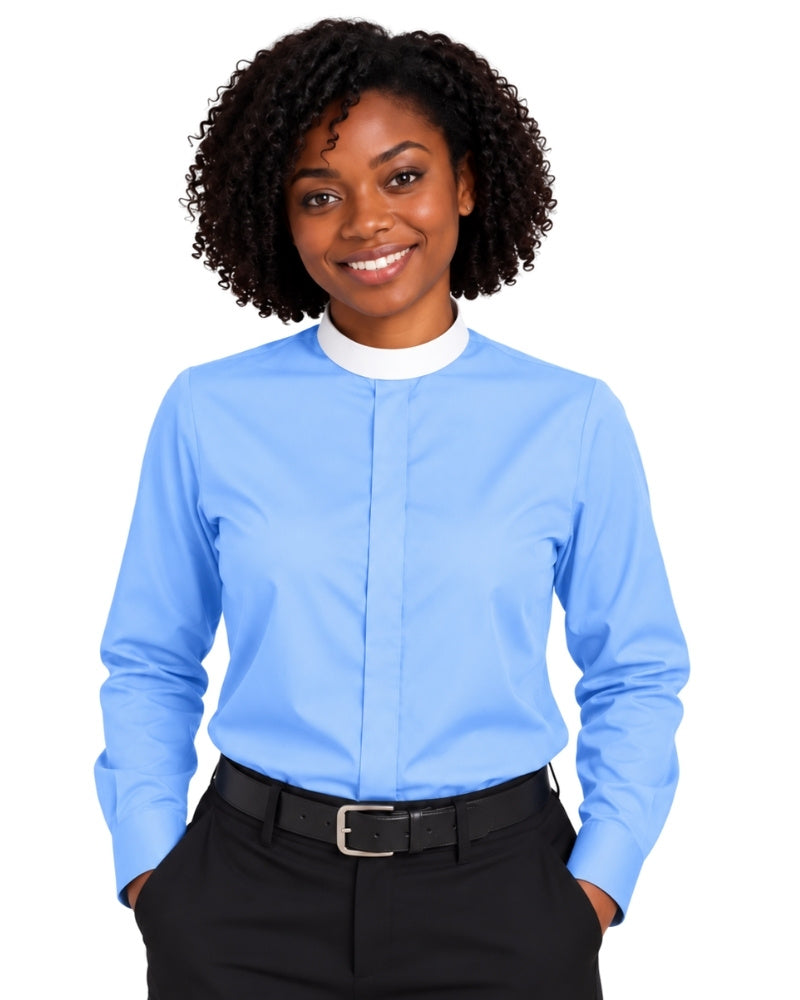 A smiling woman with curly black hair wearing a light blue long-sleeve clerical shirt with a white mock neck collar, paired with black trousers and a black belt, against a plain white background.