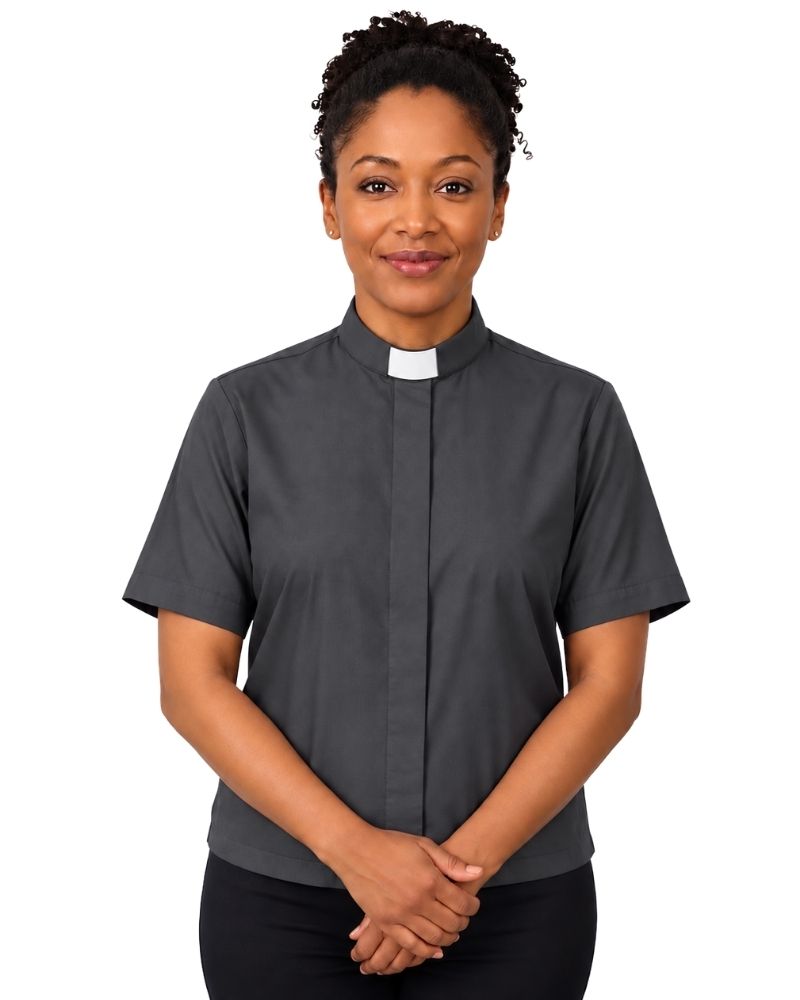 A woman wearing a dark gray short-sleeve clerical shirt with a white collar, standing against a plain white background.
