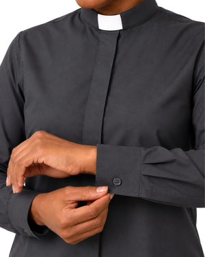 A close-up of a woman wearing a dark charcoal gray long-sleeve clerical shirt with a white collar, adjusting the cuff.