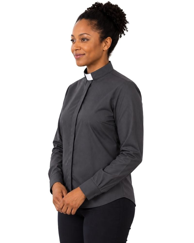 A woman wearing a dark gray long-sleeve clerical shirt with a white collar, standing against a plain white background.