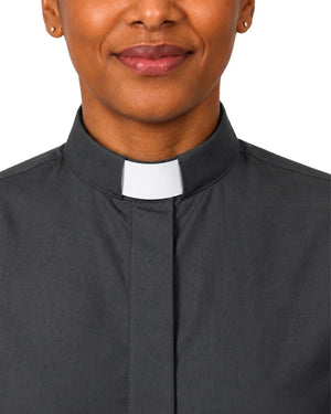A close-up of a woman wearing a dark charcoal gray clerical shirt with a white clerical collar, set against a plain white background.