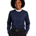 A woman with curly black hair wearing a navy blue long-sleeve clerical shirt with a white mock neck collar, paired with black trousers and a black belt, against a plain white background.