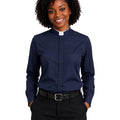 A smiling woman with curly black hair wearing a navy blue long-sleeve clerical shirt with a white collar, paired with black trousers and a black belt, against a plain white background.