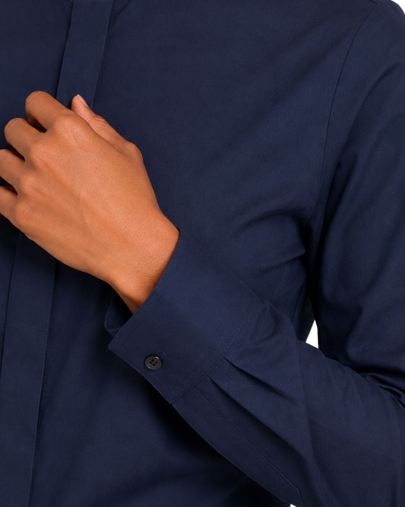Close-up of a women wearing a dark navy long-sleeve clerical shirt, with one hand adjusting or touching the collar area near the chest.