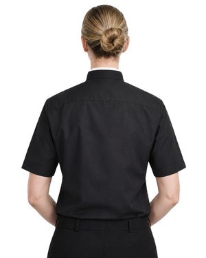 Rear view of a woman wearing a black short-sleeve clergy shirt with a stand collar, paired with black trousers, against a plain white background.