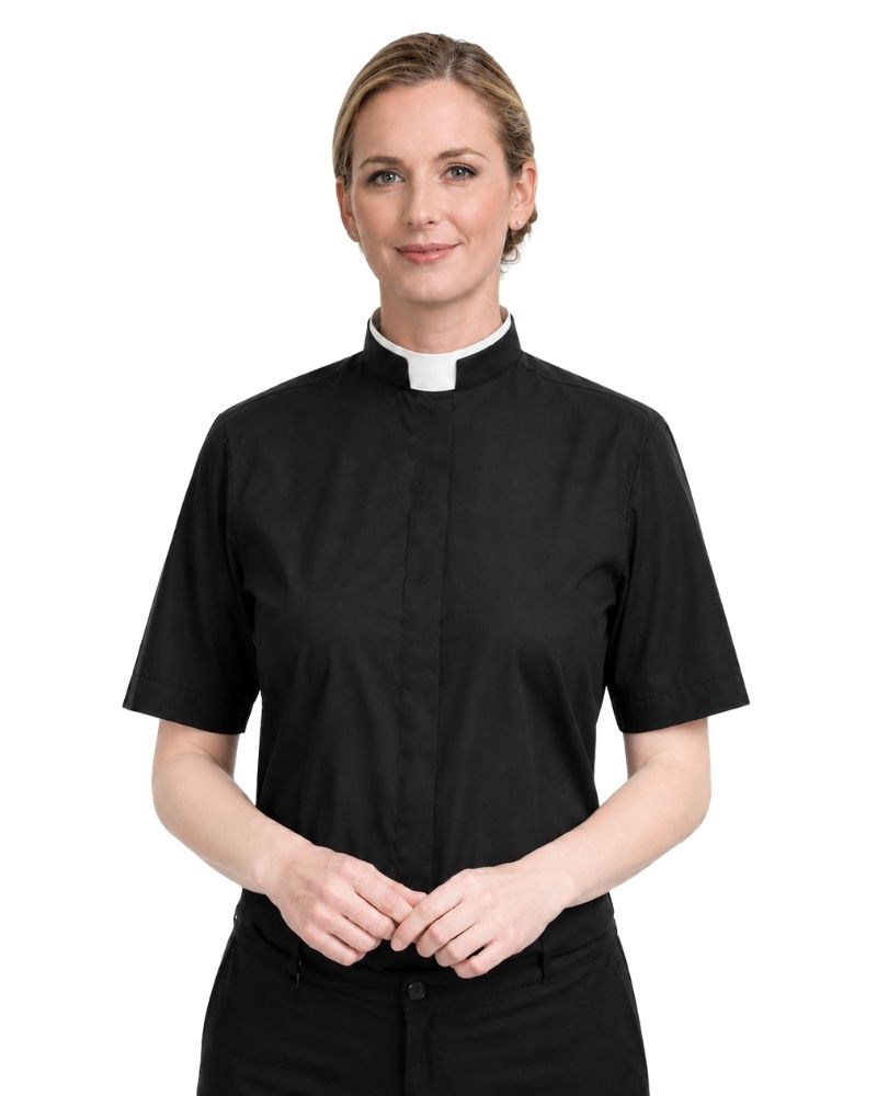 A woman wearing a black short-sleeve clerical shirt with a white collar, standing against a plain white background.