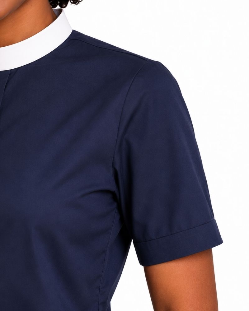 Close-up of a navy blue short-sleeve clerical shirt with a contrasting white collar, worn by a model against a plain white background.