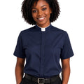 A smiling woman with curly black hair wearing a navy blue short-sleeve clerical shirt with a white collar, paired with black trousers and a black belt, against a plain white background.