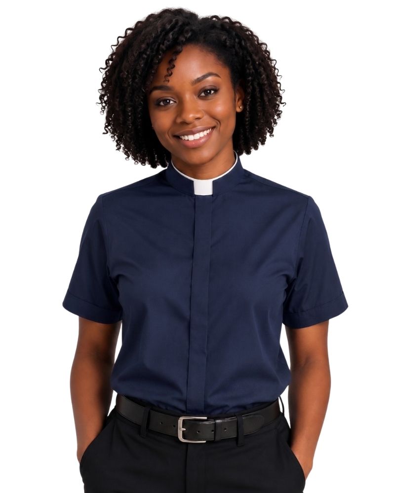 A smiling woman with curly black hair wearing a navy blue short-sleeve clerical shirt with a white collar, paired with black trousers and a black belt, against a plain white background.