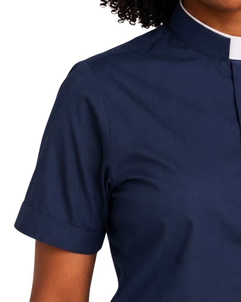 A close-up of a navy blue short-sleeve clerical shirt with a white collar trim, worn by a model against a plain white background.
