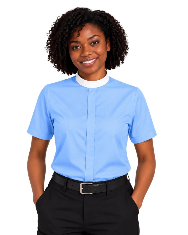 A smiling woman with curly black hair wearing a light blue short-sleeve clerical shirt with a white mock neck collar, paired with black trousers and a black belt, against a plain white background.