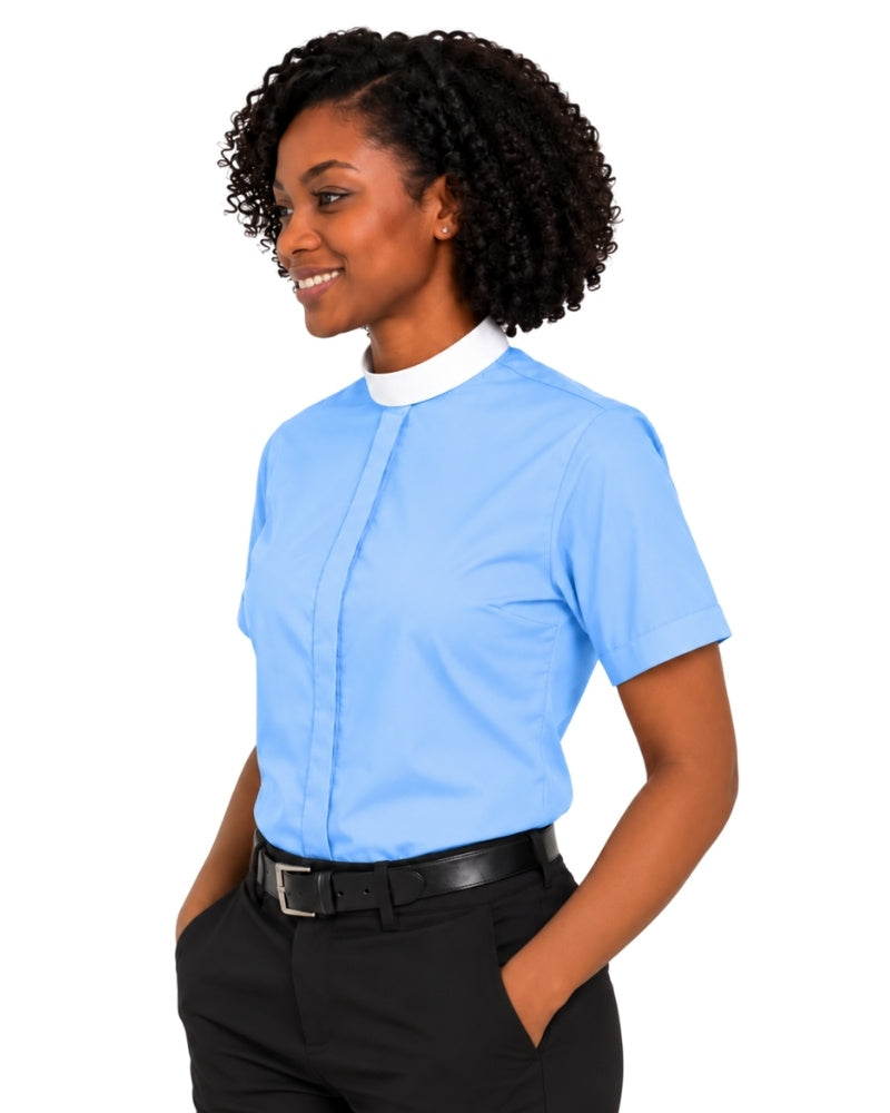 A woman with curly black hair wearing a light blue short-sleeve clerical shirt with a white collar, paired with black trousers and a black belt, shown from the waist up against a plain white background.