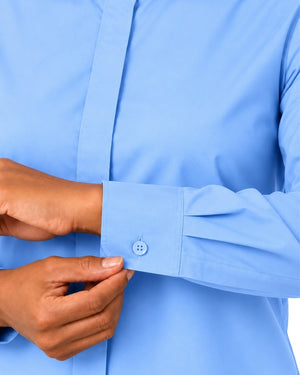 A close-up of a woman hands adjusting the cuff of a light blue long-sleeve clerical shirt, showing the buttoned cuff and fabric texture.