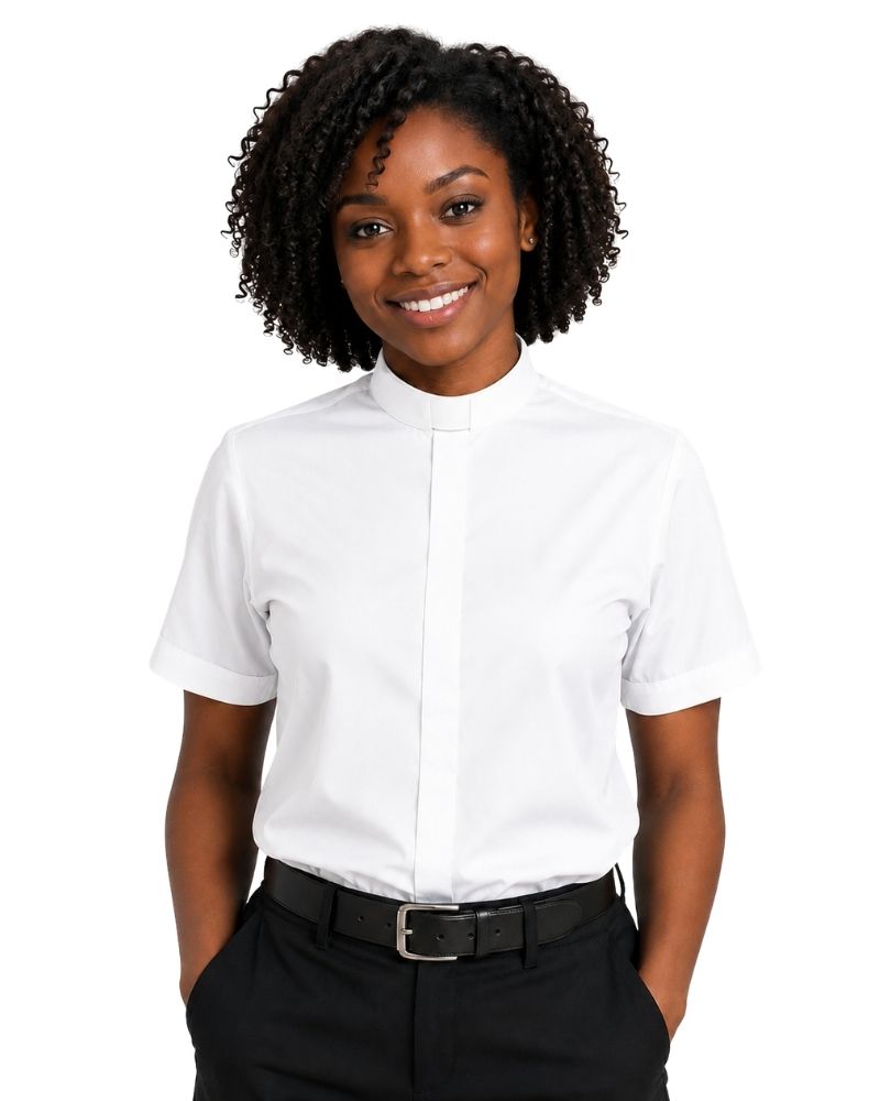 A smiling woman with curly black hair wearing a white short-sleeve clerical shirt with a high mock neck, tucked into black trousers with a black belt, against a plain white background.
