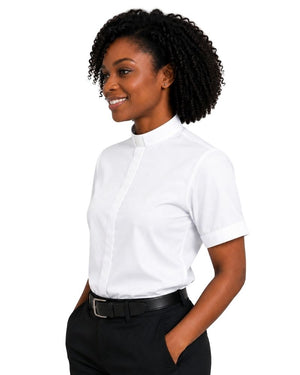 A woman with curly black hair wearing a white short-sleeve clerical shirt with a high mock neck, paired with black trousers and a black belt, shown from a side profile against a solid white background.