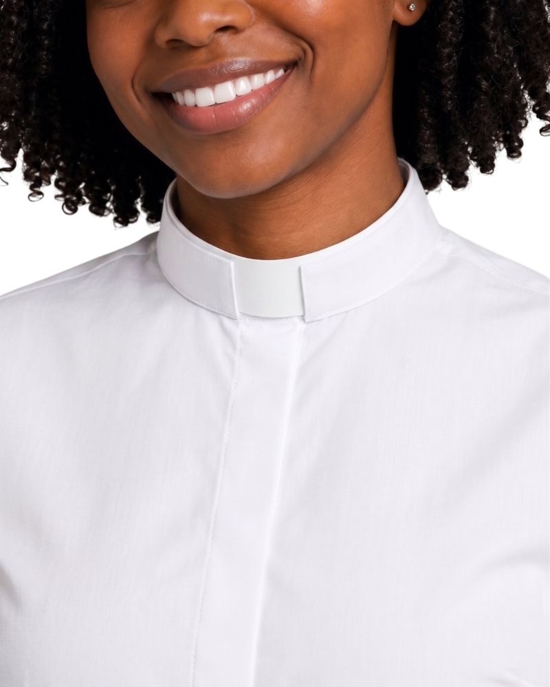 A close-up of a smiling women wearing a white collared shirt with a clerical collar, shown against a plain white background.
