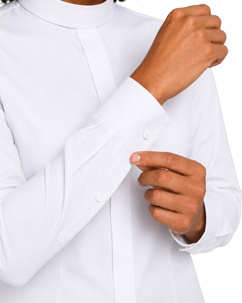 A close-up of a women wearing a white long-sleeve clerical shirt, adjusting the cuff with one hand while the other hand rests near the front button.