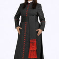 Woman wearing a long black coat with red buttons and fringes on a white background