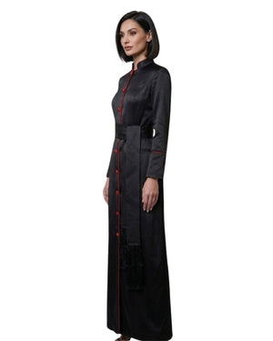 A woman modeling a long black robe with red trim and red buttons, shown in profile against a plain white background.