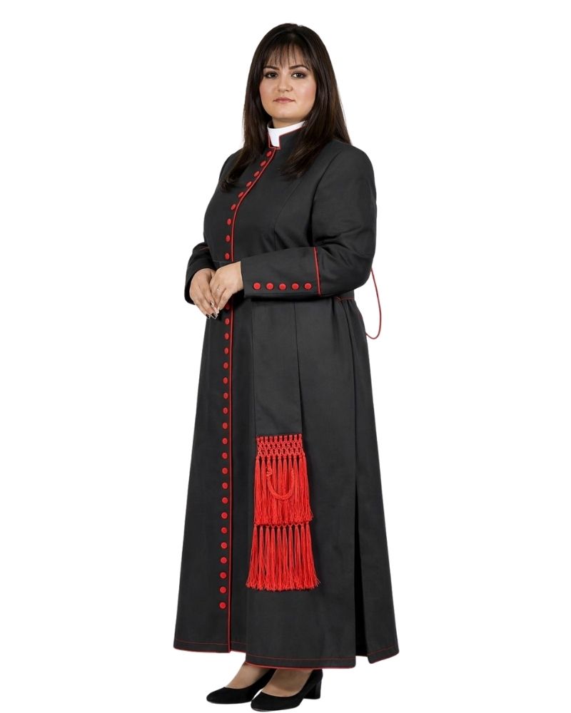 A woman modeling a long black clerical cassock with red trim, red decorative buttons, and a red tassel detail, shown against a plain white background.