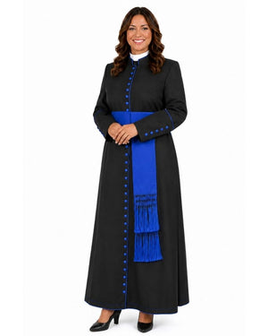 A woman modeling a long black cassock with a bright royal blue sash, blue decorative buttons, and a white collar, photographed against a plain white studio background.