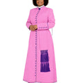 A woman modeling a long pink cassock with purple fringe and button details, set against a plain white background.