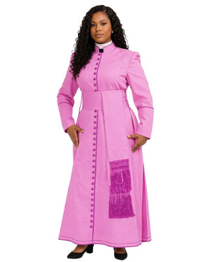 A woman modeling a bright pink long-sleeve cassock with a high collar, decorative front buttons, a matching waist sash, and a purple fringe detail on the skirt, set against a plain white background.