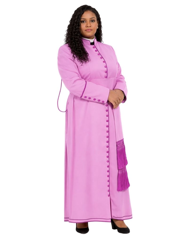 A woman modeling a long pink cassock with matching pink buttons, a high collar, and a purple tassel detail on the front, set against a plain white background.