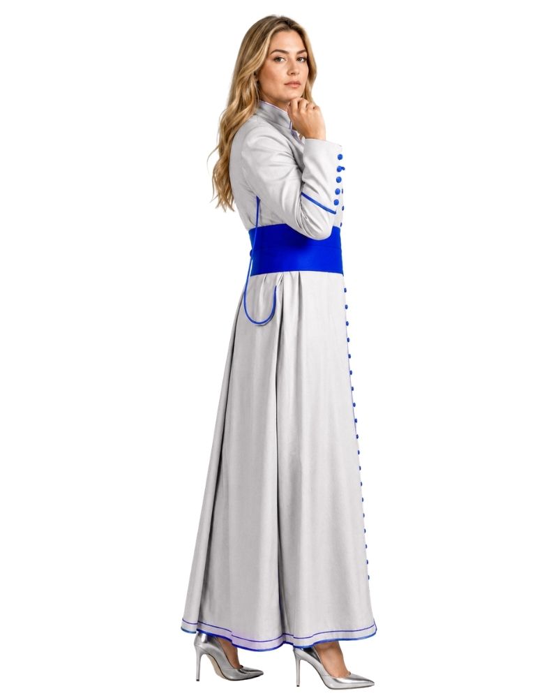A woman modeling a long white cassock with a bright blue waistband, blue trim details, and blue buttons, paired with silver high heels, set against a plain white background.