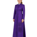 Woman wearing a long purple cassock with a white collar on a white background.