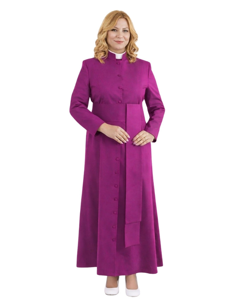 A woman modeling a long magenta-purple clerical robe with a high collar, front buttons, and a matching waist tab, worn over a white collar, on a plain white background.