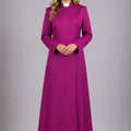 Woman wearing a long purple dress with a white collar against a gray background