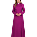 A woman wearing a long magenta-purple clerical robe with a white collar, standing against a white background.