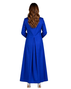 A woman viewed from behind wearing a long royal blue cassock with long sleeves and a gathered back seam, shown against a plain white background.