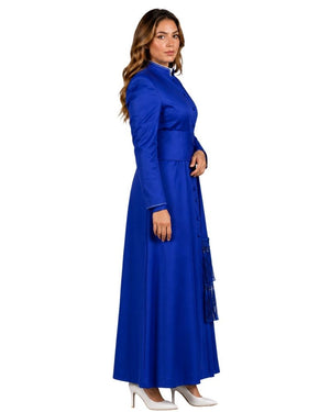 A woman modeling a long royal blue cassock with long sleeves, a high collar, and a fitted waist, shown in profile against a plain white background.