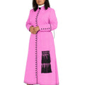 A woman modeling a bright pink cassock with black fringe and black decorative buttons, styled with a white collar and black heels, against a plain white background.