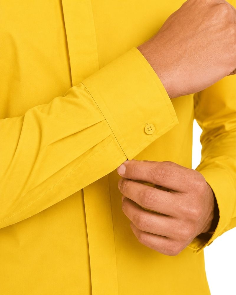 Close-up of a man wearing a bright yellow long-sleeve clerical shirt, adjusting the cuff with one hand while the other hand rests near the front.
