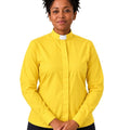 A woman wearing a bright yellow long-sleeve clerical shirt with a white collar tab, paired with black pants, standing against a plain white background.
